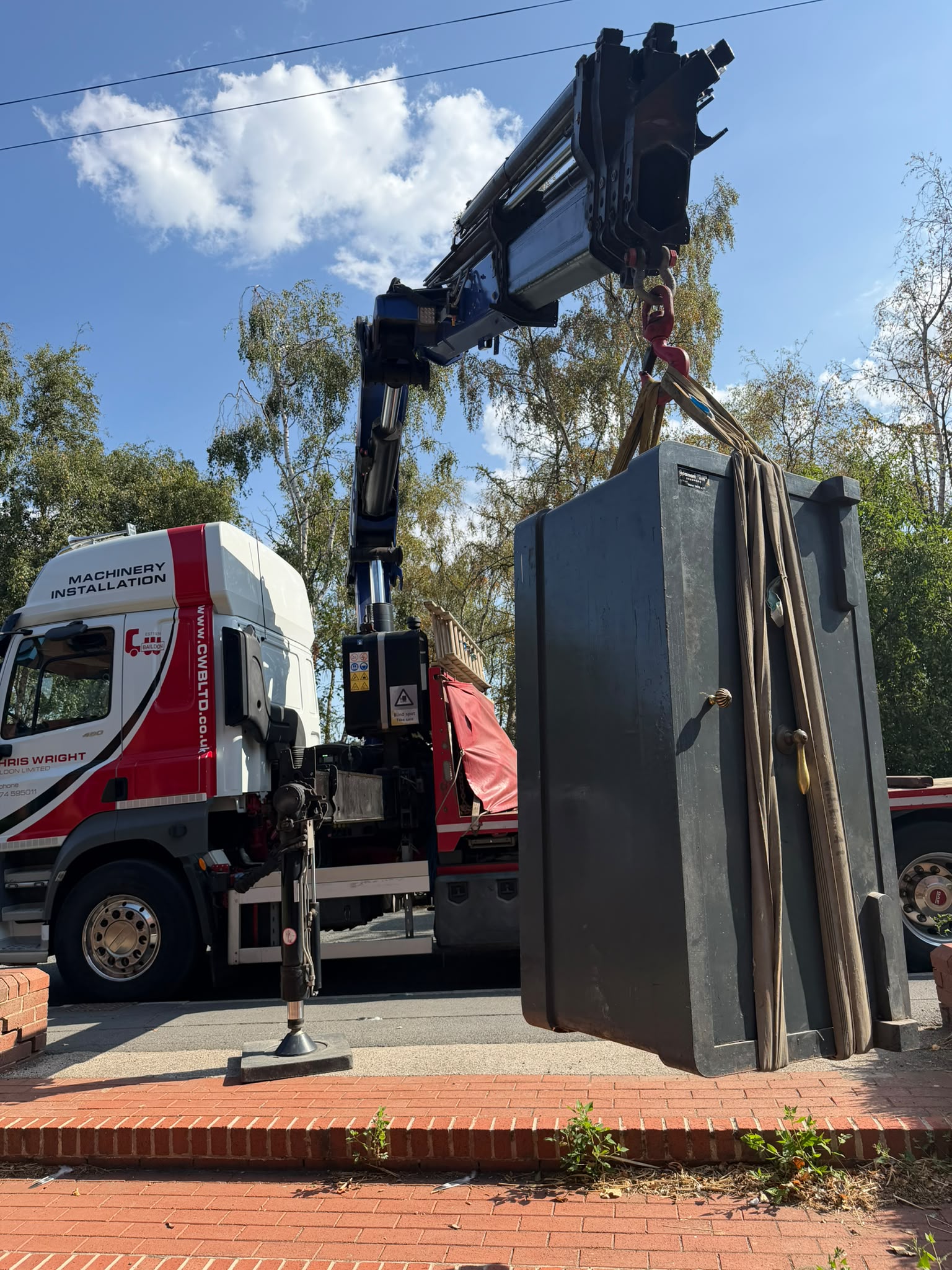 A heavy safe being lifted onto specialist transport with a vehicle-mounted crane